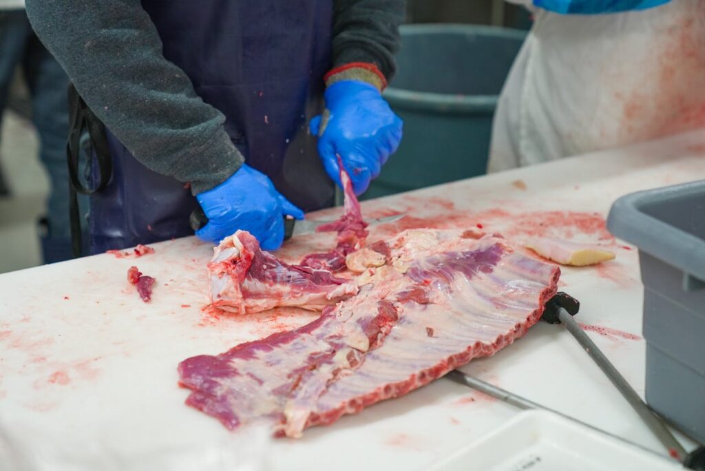 Close-up of a butcher processing meat with gloves on, highlighting food preparation techniques.